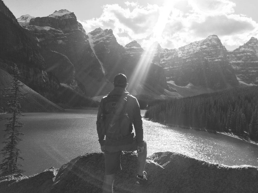 Person sitting on a rock by a serene lake with mountains in the background.